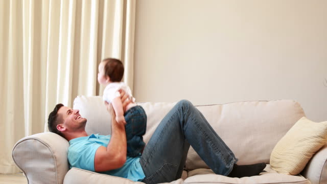Padre-jugando-con-su-bebé-niño-en-el-sofá-en-la-sala-de-estar