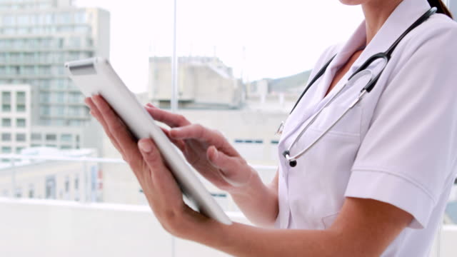 Nurse-in-tunic-using-tablet-pc-and-smiling-at-camera