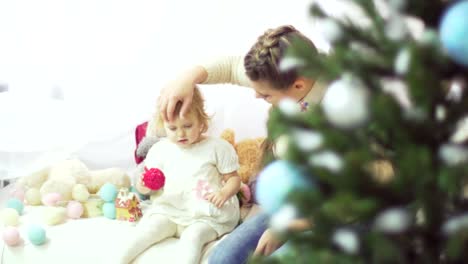Glückliche-junge-Mutter-mit-ihrem-süßen-Baby-in-einem-eingerichteten-Raum-in-der-Nähe-der-Weihnachtsbaum-spielen