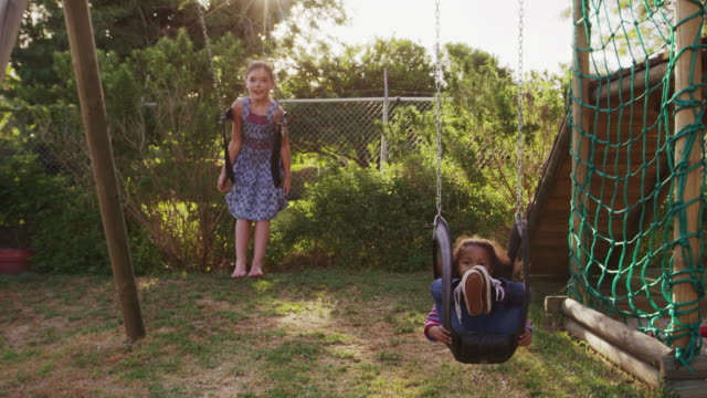 Dos-chicas-jugando-al-aire-libre-en-casa-en-los-columpios-del-jardín