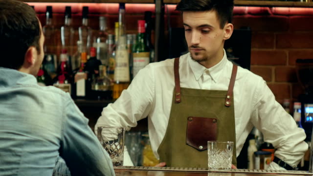 Young-bartender-talking-and-smiling-to-a-male-visitor