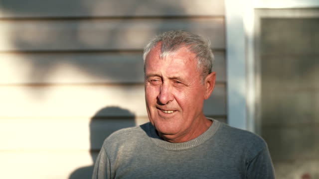 Close-up-portrait-of-smiling-old-man-looking-at-the-camera,-laughing-retired-male-standing-in-front-of-sun.-4K