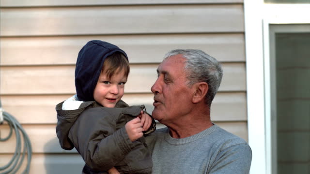 Grandfather-and-grandson-talking,-smiling,-having-fun,-looking-to-camera-outdoor.-Old-man-holding-on-hand-little-boy.-4K