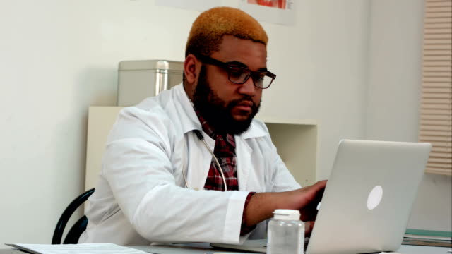 Doctor-masculino-americano-africano-trabajando-en-ordenador-portátil-en-su-escritorio