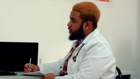 Afroamerican-doctor-talking-to-the-patient-and-taking-notes