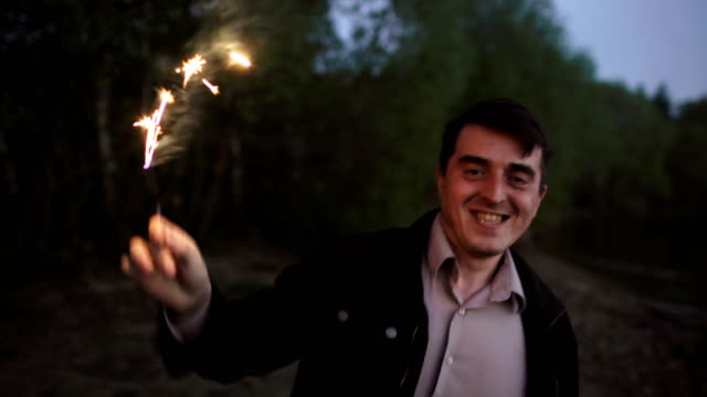 Portrait-of-young-smiling-man-with-sparkler-celebrating-at-beach-party
