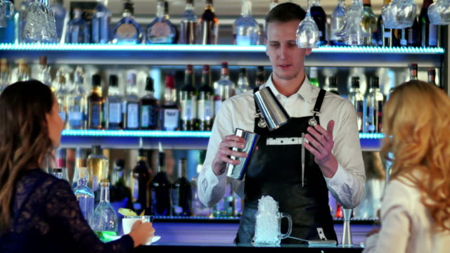 Barkeeper-macht-cocktail-am-Tresen-für-zwei-Mädchen