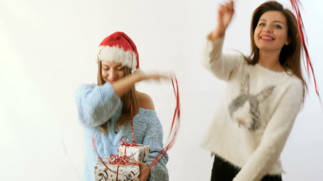 Two-girlfriends-waving-a-red-ribbons-and-dances-with-gifts-at-white-background