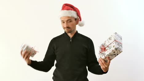 Mann-in-der-Weihnachtsmütze-vergleicht-zwei-Geschenke-in-Händen-auf-weißem-Hintergrund