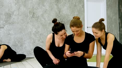 Drei-junge-Frauen,-die-mit-digitalen-Handy-nach-Training-im-Yoga-Kurs
