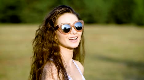 Mujer-joven-con-gafas-de-sol-y-posando-felizmente-en-naturaleza-mirando-lejos-de-luz-del-sol