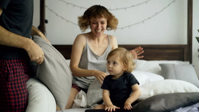 Glückliche-Familie-mit-kleinen-niedlichen-Tochter-spielen-und-kämpfen-Kissen-im-Bett-zu-Hause