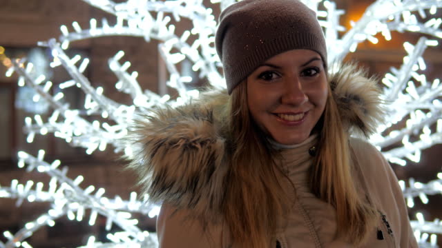 Junge-Frau-In-warme-Kleidung,-Lächeln,-stehen-inmitten-von-Weihnachtsbeleuchtung