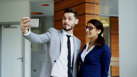 Happy-businessman-and-his-female-colleague-taking-a-selfie-on-smarphone-camera-for-social-media-in-modern-office
