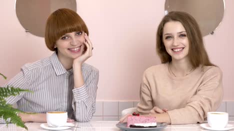 Zwei-junge-kaukasische-Mädchen-sitzen-in-einem-Café-und-lächelt-in-die-Kamera-schaut-Porträt.-Mädchen-in-einem-Café-Konzept.-60fps