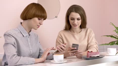 Two-young-Caucasian-girls-sitting-in-a-cafe-and-smiling,-using-a-smartphone,-texting,-typing.-The-girls-are-in-a-cafe.-60-fps