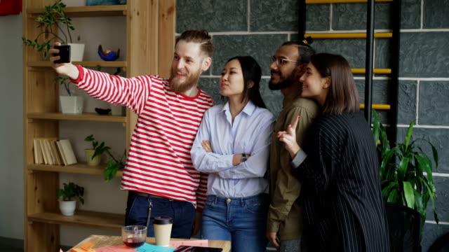 Glücklich-multiethnischen-Team-nehmen-Selfie-im-modernen-Loft-Büro.-Hipster-Mann-Betrieb-Smartphone-nehmen-Selbstporträt-mit-seinen-Kollegen