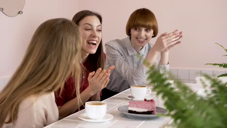 Three-young-Caucasian-girls-sitting-in-a-cafe,-drinking-coffee,-eating-cake,-smiling,-laughing,-gesturing-with-their-hands,-old-girlfriends-in-a-cafe-concept.-60-fps