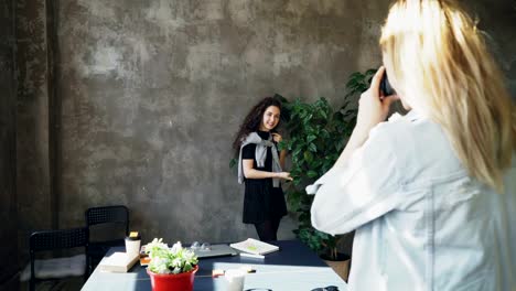 Attraktive-Mädchen-posiert-mit-großen-Anlage-während-Kollegin-Photogrpahing-ihr-Digitalkamera-in-modernen-Lof-Büro-auf.-Frauen-sind-Spaß-und-lachen-während-der-Kaffeepause