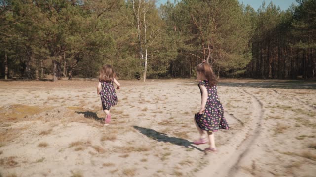 zwei-Mädchen-laufen-auf-Sand-in-einem-Sommer-Wald