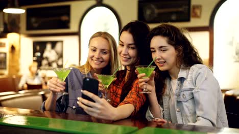 Attraktive-junge-Frauen-nehmen-Selfie-mit-Cocktails-in-der-Bar.-Fröhliche-Mädchen-posieren,-lachen-und-Gläser-Klirren.-Fotografieren-für-Instagram-Account-Konzept.