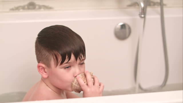 Two-little-boys-having-fun-with-seashell-while-taking-bath-in-bathtub