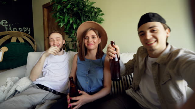 Point-of-view-shot-of-cheerful-friends-taking-selfie-with-beer-bottles,-posing-and-smiling,-laughing-and-gesturing.-Friendship-and-happy-young-people-concept.