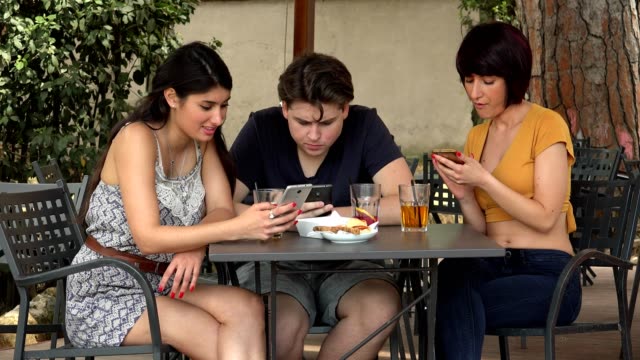 young-people,-smartphones---three-friends-at-the-cafe-focused-on-their-smartphones