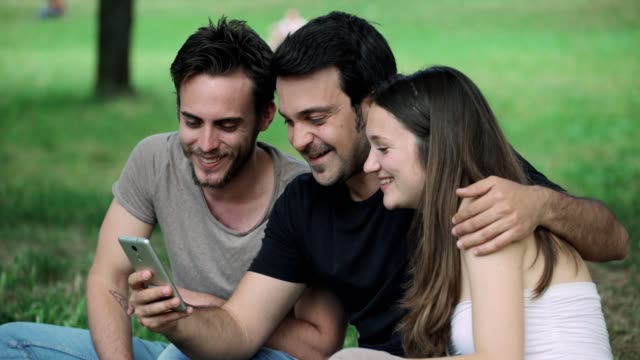 Freunde-konzentriert-sich-auf-Blick-auf-Smartphone-im-Park-Glück,-Freude,-Entspannung