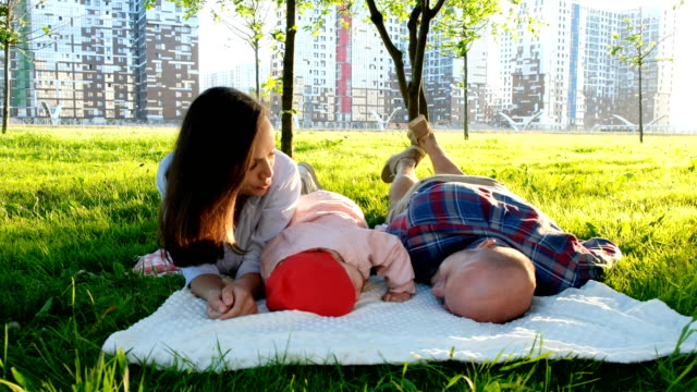 Vater-und-Tochter-liegen-mit-Mutter-auf-dem-Rasen-im-Park-im-Sommer.-Glückliche-Familie-mit-Baby-ruht-im-Sommerpark-bei-Sonnenuntergang