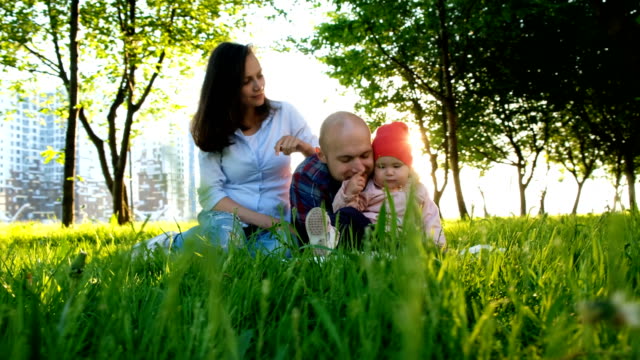 Happy-family-is-resting-on-nature.-Parents-play-with-a-small-baby-daughter-in-a-park-in-the-summer-at-sunset,-camera-movement