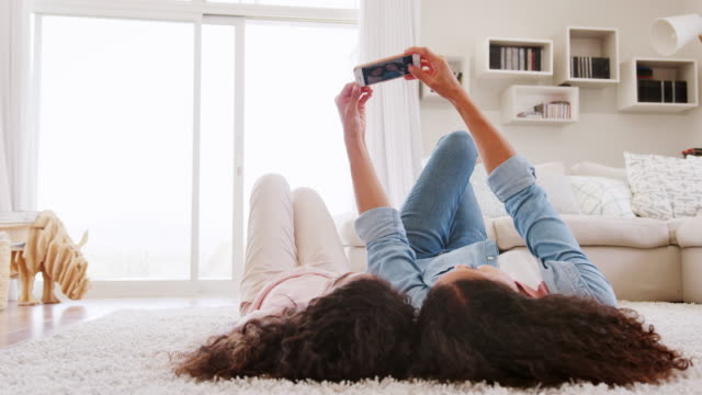 Mutter-und-Tochter-auf-Teppich-liegend-und-posieren-für-Selfie-zu-Hause