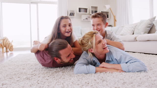 Portrait-Of-Children-Lying-On-Parents-Backs-On-Rug-In-Lounge-At-Home-Shot-In-Slow-Motion
