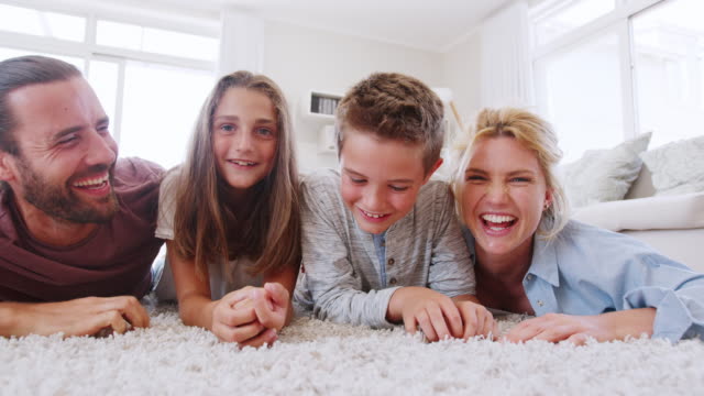 Portrait-Of-Family-Lying-On-Rug-In-Lounge-At-Home-Shot-In-Slow-Motion