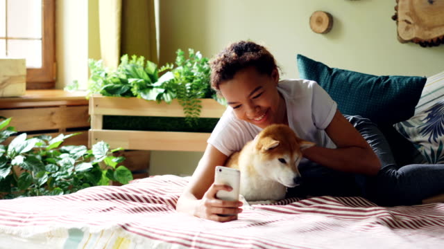 Freudige-Hundebesitzer-nimmt-Selfie-mit-niedlichen-Haustier-auf-Bett-zusammenhält-Smartphone-zu-posieren-und-umarmt-Tier-liegen.-Freundschaft-zwischen-Menschen-und-Welpen-Konzept.