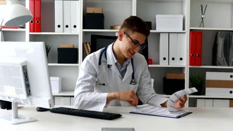 Young-doctor-researching-documents-and-smiling-at-camera