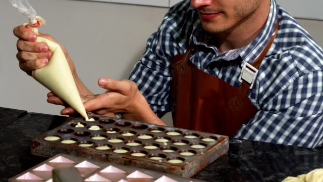 Joven-macho-pastelería-agregar-vainilla-relleno-en-los-moldes-de-chocolate-caramelo