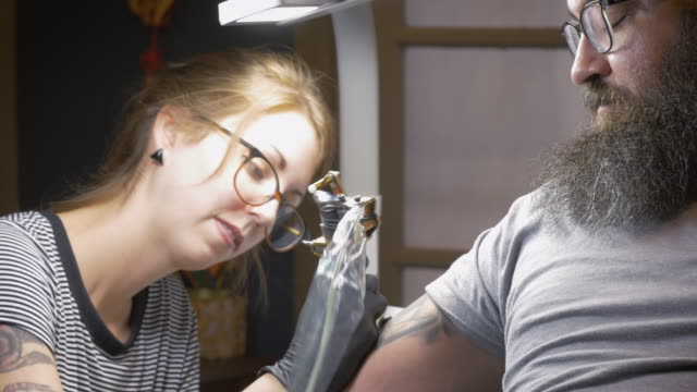 Female-Tattoo-Artist-Tattooing-a-Bearded-Male-Client-in-4k