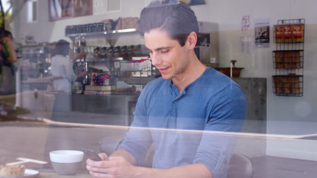Junge-männliche-Kunden-überprüfen-sein-Smartphone-in-einem-Coffee-shop