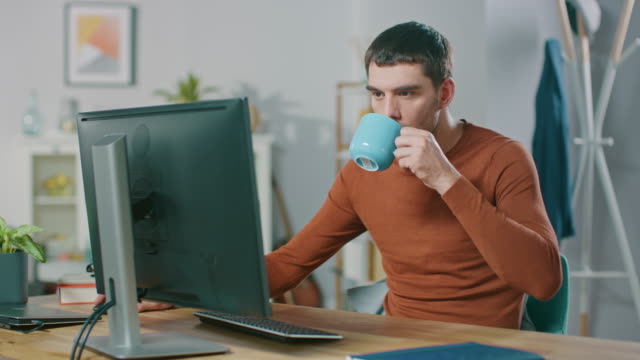 Portrait-of-Handsome-Confident-Man-Working-on-a-Personal-Computer-from-Home.-In-Cozy-Bright-Living-Room-Man-Browses-Through-Internet.