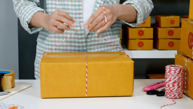 Hand-der-Unternehmerin-sind-Seile-binden-und-Verpackung-von-Produkten-in-Paketbox,-vorbereiten-für-die-Auslieferung-an-Kunden-im-home-office