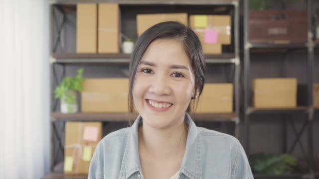 Business-Frau-glücklich-lächelnd-und-Blick-auf-Kamera-während-der-Arbeit-in-ihrem-Büro-zu-Hause.-Schöne-asiatische-junge-Unternehmer-Eigentümer-der-KMU-mit-kleinen-Unternehmer-im-home-Office-Konzept.