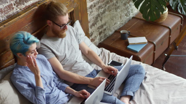 Hipster-paar-mit-Laptops-arbeiten-aus-dem-Bett