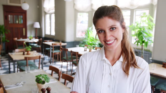 Portrait-Of-Waitress-Standing-In-Empty-Restaurant-Before-Start-Of-Service