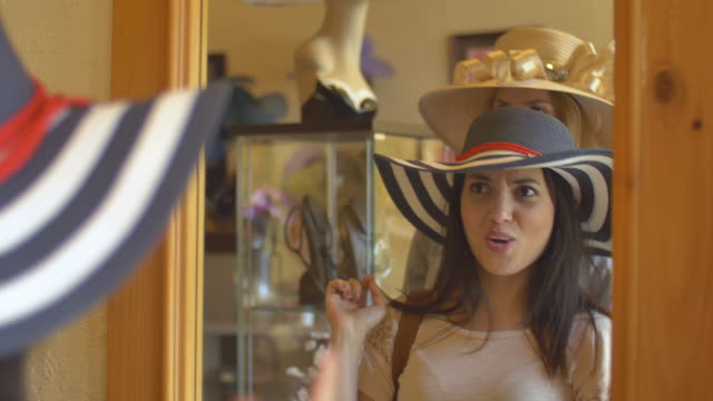 Dos-mujeres-jóvenes-tratando-en-sombreros-en-una-tienda-y-mirando-en-un-espejo
