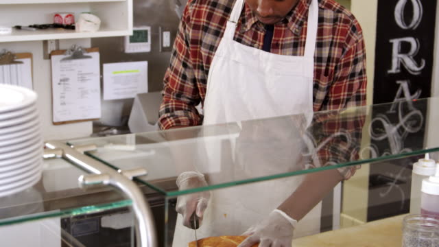 Man-slicing-bread-behind-the-counter-of-a-sandwich-bar,-shot-on-R3D