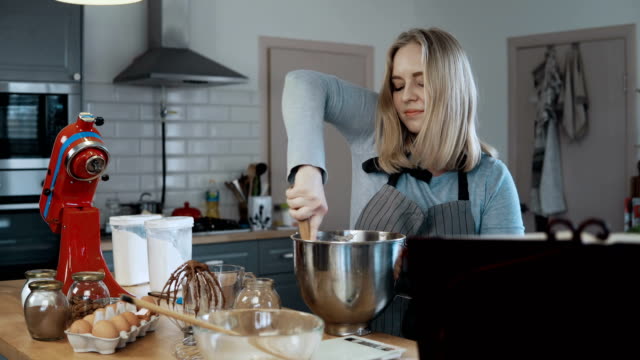 Young-beautiful-woman-mixing-the-ingredients-in-a-bowl,-preparing-dough-for-baking.-Blonde-female-in-kitchen