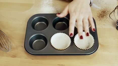 Close-up-view-of-female-hand-putting-the-paper-cups-into-the-baking-tray.-Woman-cooking-cupcakes.-Time-lapse