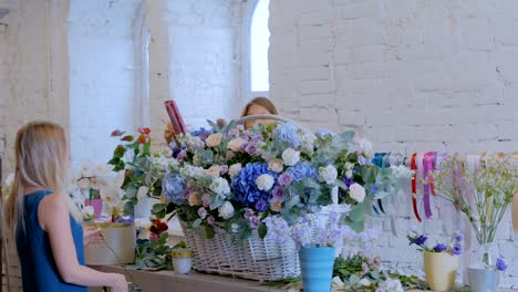 Floristas-de-dos-mujeres-haciendo-la-gran-cesta-de-flores-con-flores-en-la-tienda-de-la-flor