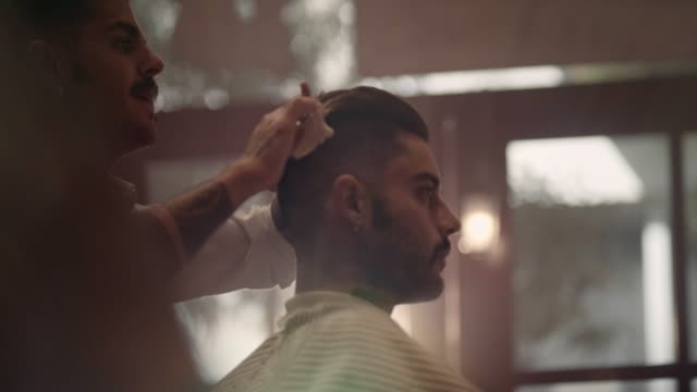 Young-stylish-barber-with-tattoos-cutting-and-styling-man's-hair